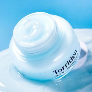 Close-up of a white Torriden soothing cream jar with light blue cream, against a blue background.