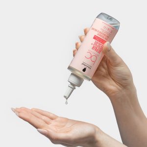 Pink dropper bottle of skincare serum dispensing a drop onto a cupped hand