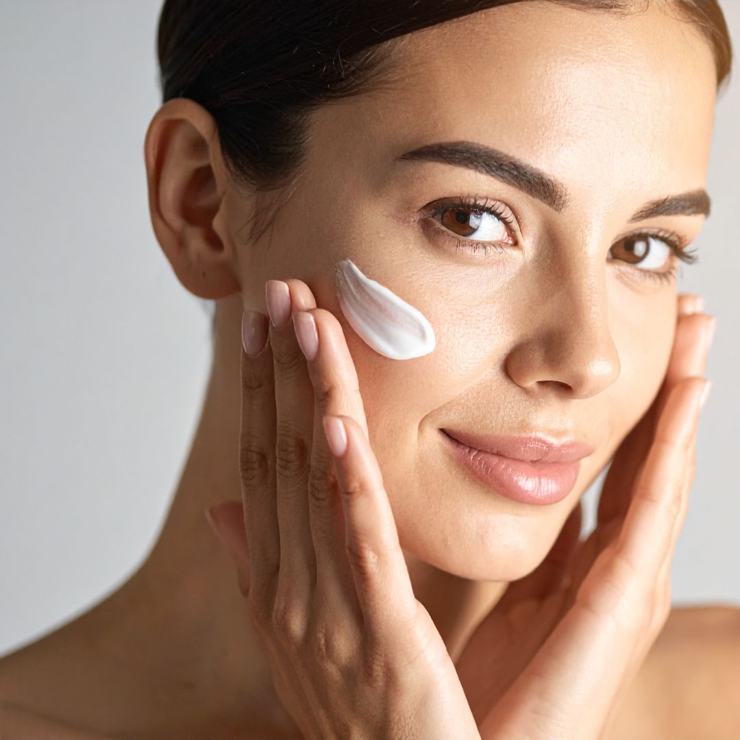 Close-up of a woman applying a thick white facial cream to the cheek with two hands.